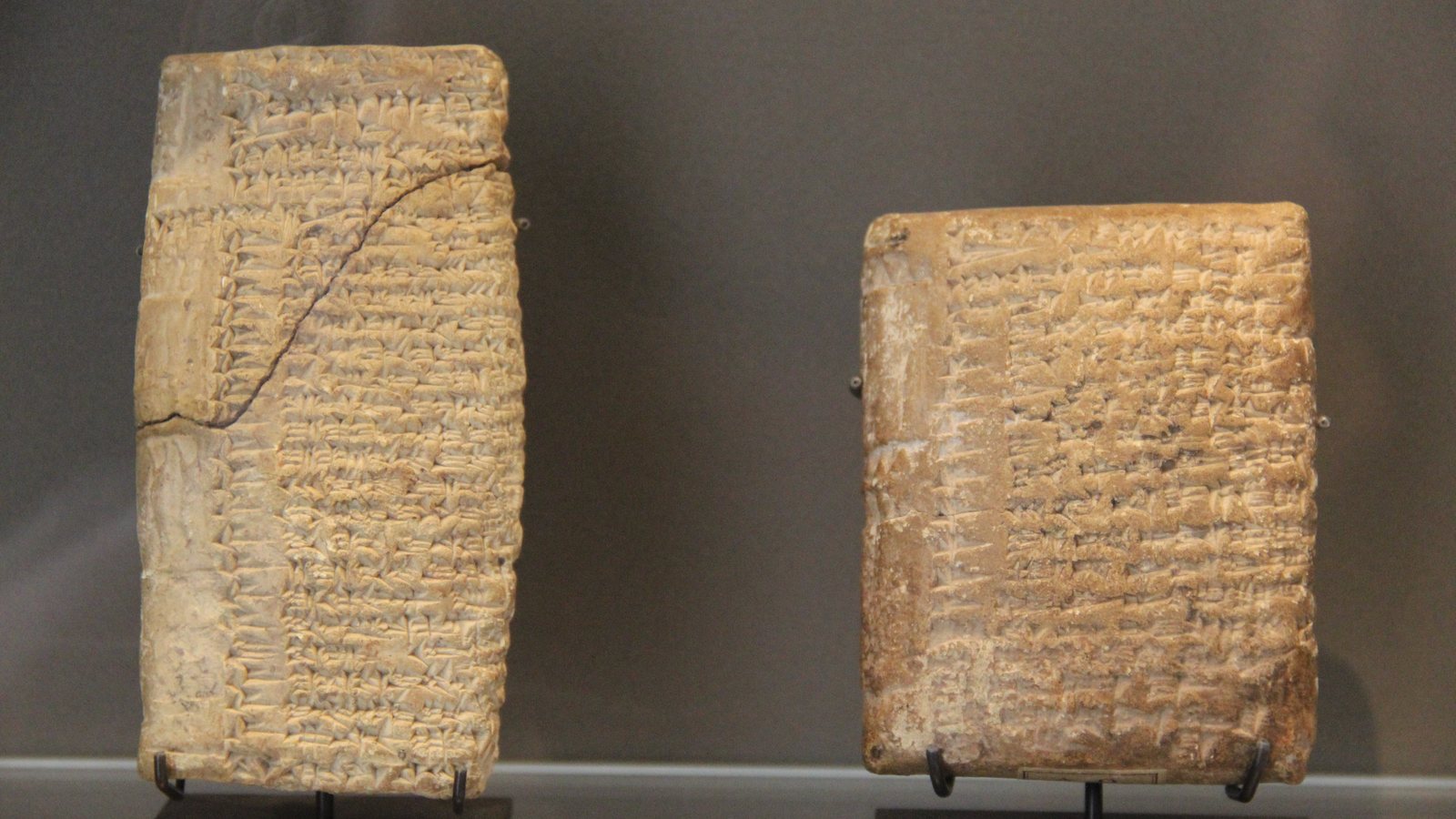 Two clay tablets covered in dense cuneiform script, lit against a dark ground
