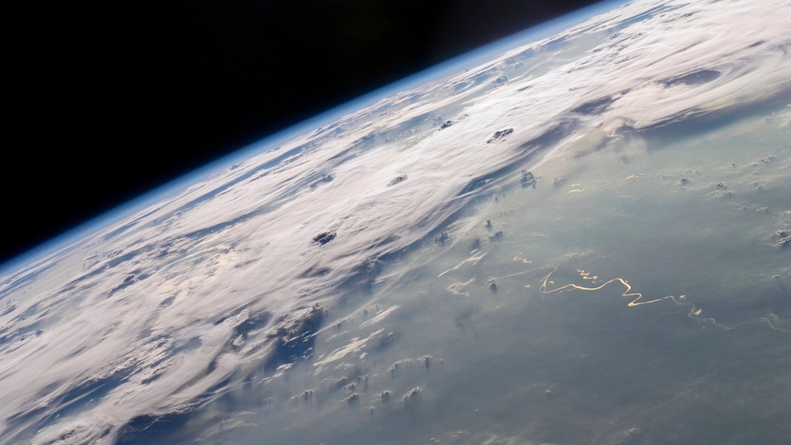 The curve of Earth seen from orbit, cloud tops and thin atmosphere along the horizon