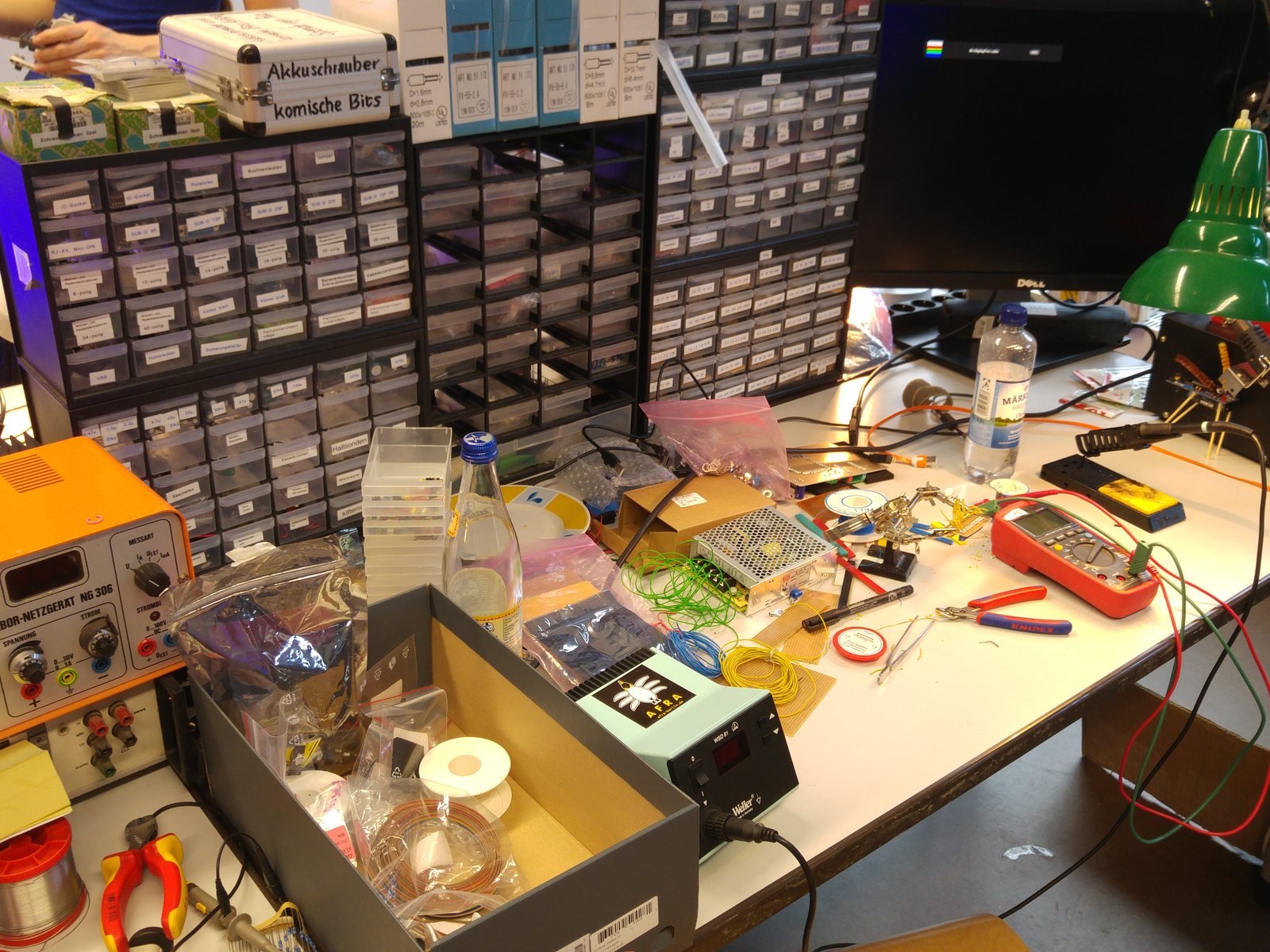 A crowded electronics workbench with hand tools, component drawers and parts trays